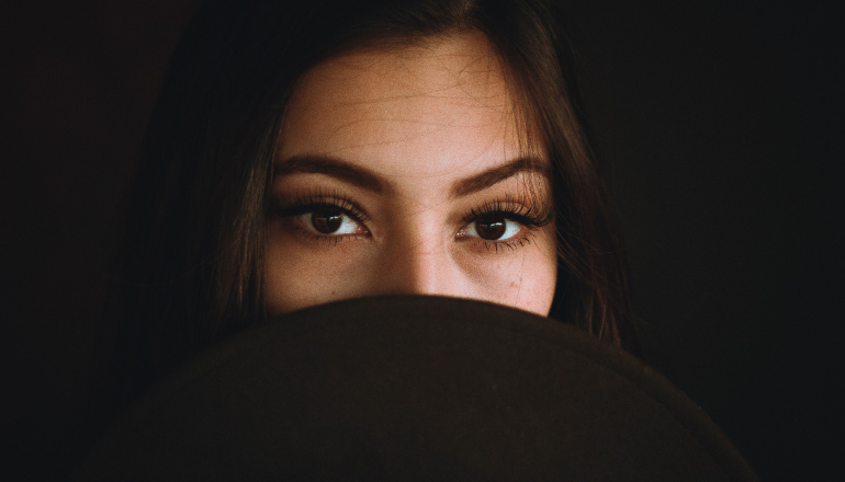 Brunette woman hides her mouth with the rim of a dark brown hat because she is self-conscious about bad breath