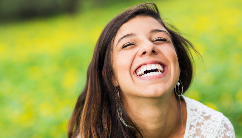 Closeup of a brunette young woman in a green field with flowers smiling with her eyes closed