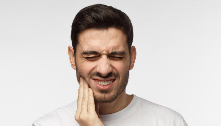 man who needs wisdom teeth extracted holds his jaw in pain
